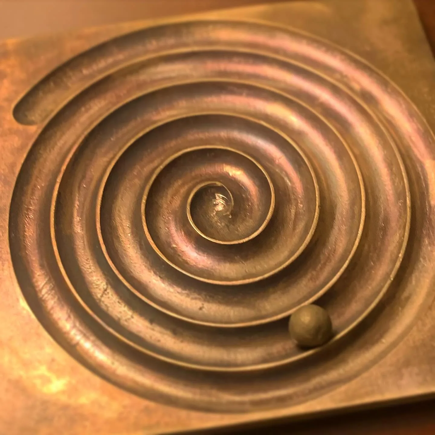 Polished copper spiral relief plate with a small clay ball under warm lamplight
