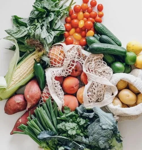 An overhead arrangement of fresh vegetables, herbs and fruit in mesh produce bags