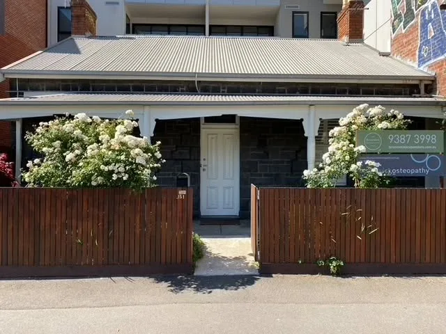 Heritage bluestone terrace frontage with white panelled door and white-flowering shrubs — the Brunswick building