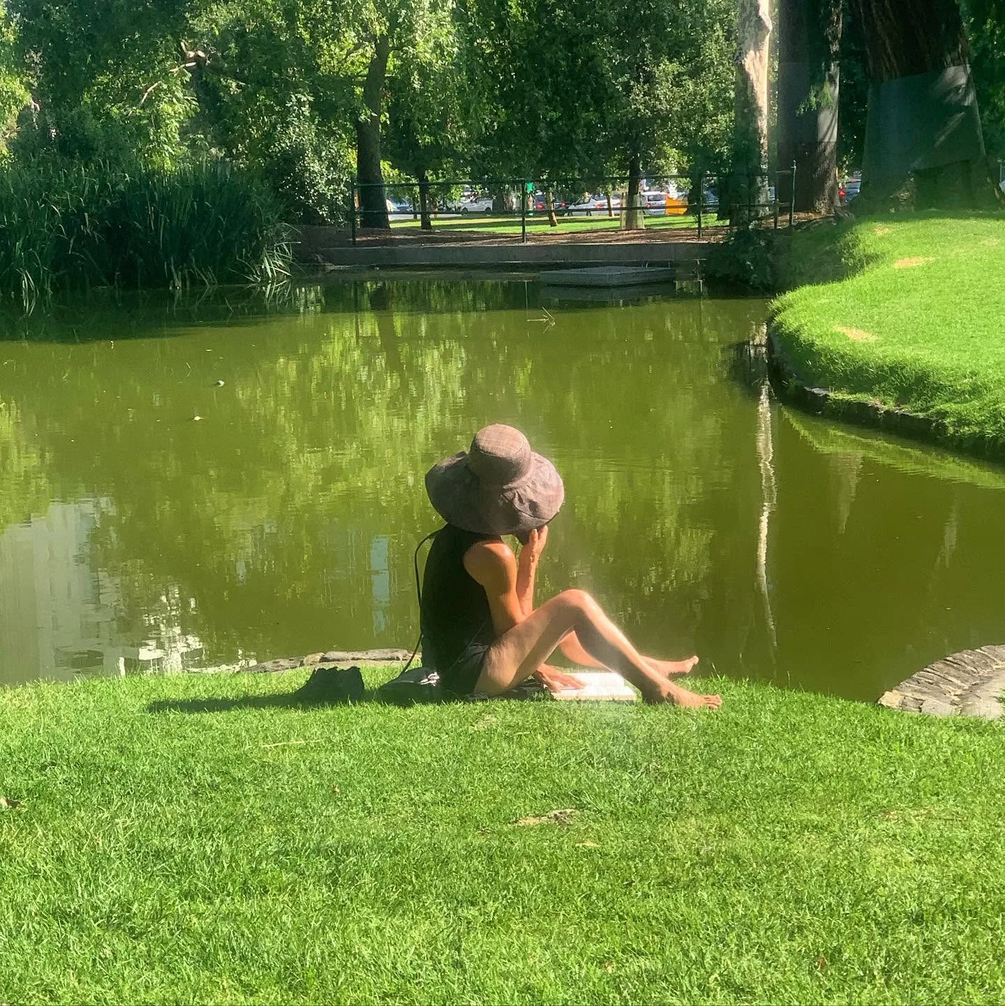 A meditative figure in a wide hat beside a still green pond — the quiet that a visit here restores